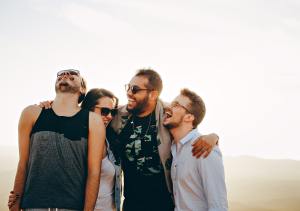 Four young students stand together, hands around each other, laughing and smiling