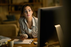 A busy student sits at her computer with her cellphone in her hand.