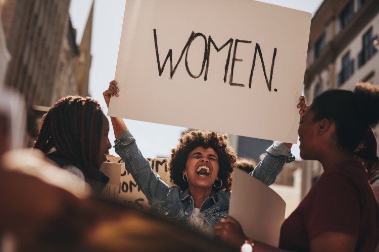 Woman holding a sign and shouting as she demonstrates with a group of women.