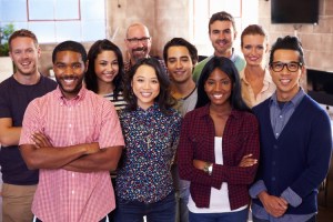 A diverse group of smiling staff members stand in their office.