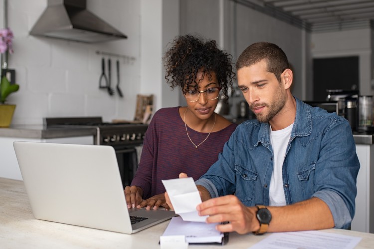 A student couple researches investment opportunities on a laptop.