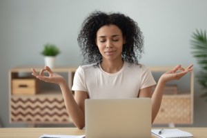 A social worker meditates while seated at a desk facing a laptop.