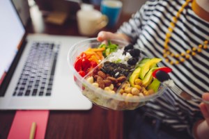 A student holds a bowl of healthy study snacks by a computer.