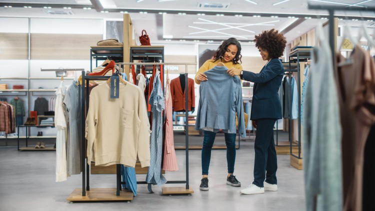 Two shoppers in a clothing store read a jacket label.