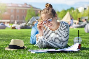 A student reads from a notebook while lying on an outdoor lawn.