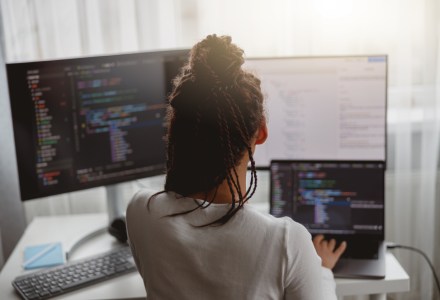 A software developer reviews code on two computer screens.