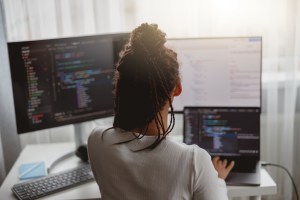 A software developer reviews code on two computer screens.