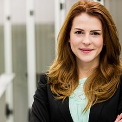 A professional woman wearing a business suit standing confidently in an office, while successfully pursuing her Masters in AI online.