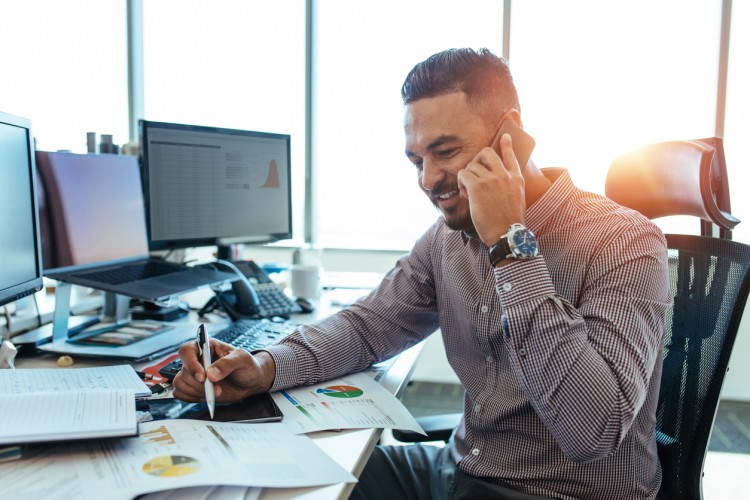 An accountant sits at a desk while talking on the phone.