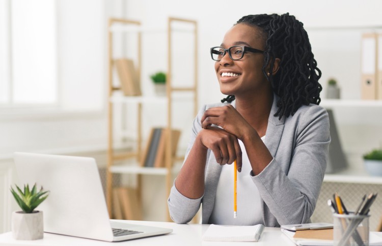 Smiling professional woman in a friendly pose sits at a desk with a laptop