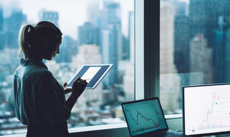 A corporate accountant looks at data while standing next to an office window.