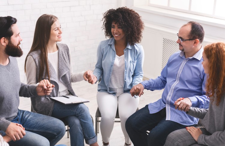 A drug and alcohol treatment specialist is holding hands with a circle of members during a group therapy session