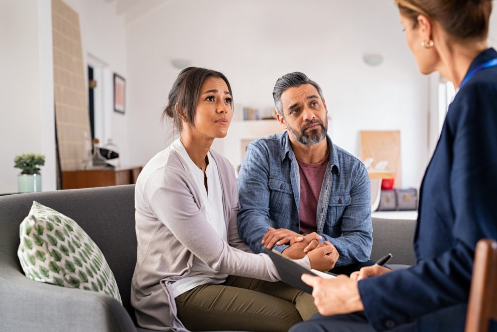 A couple sits on a couch listening to a psychologist.