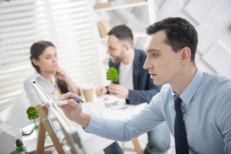 A man in the foreground works on a tablet while two people in the background talking