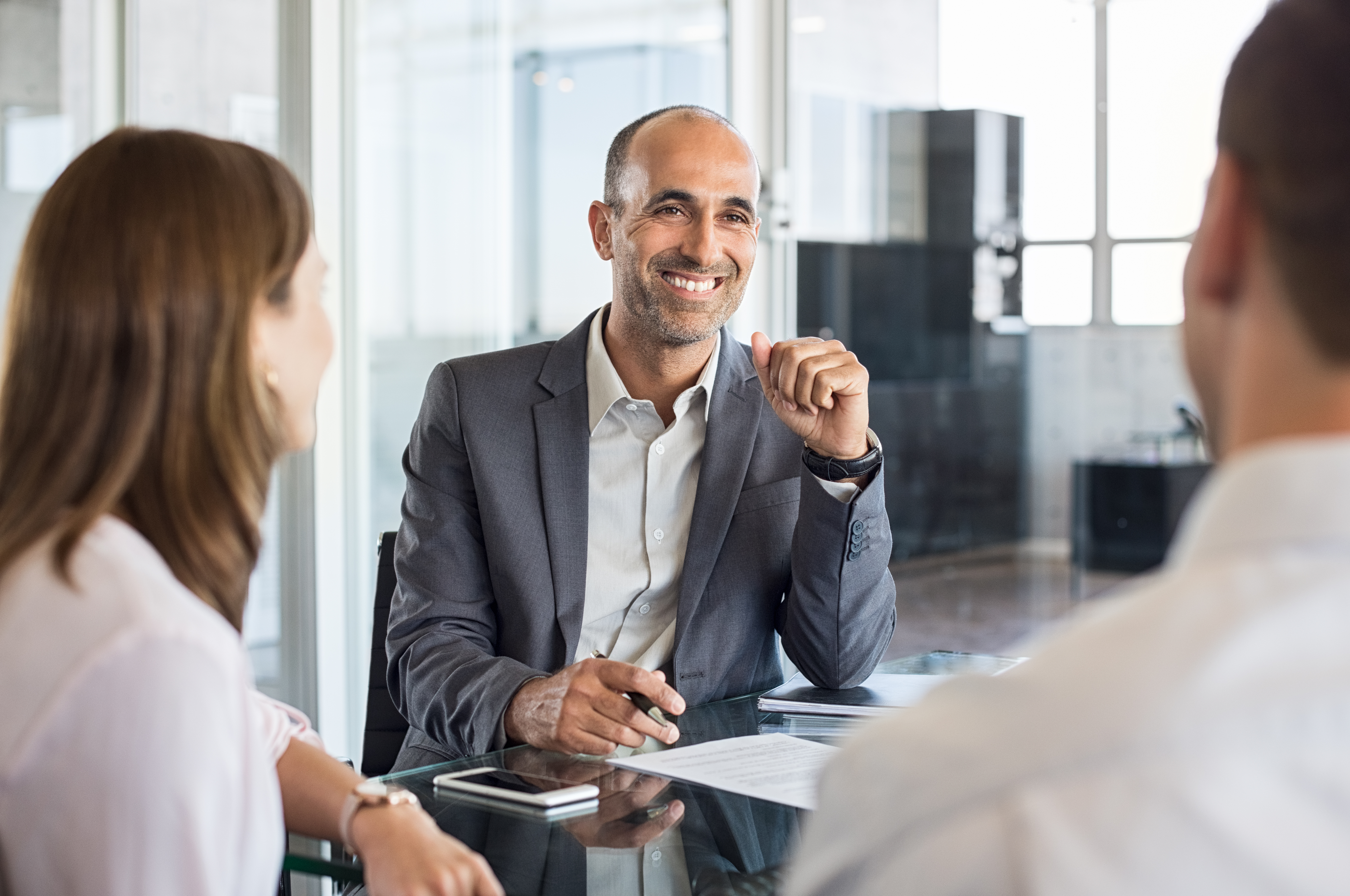 Mature financial agent in meeting sitting with young couple. Happy consultant talking with couple about their savings plan. Insurance advisor in a meeting with man and woman.