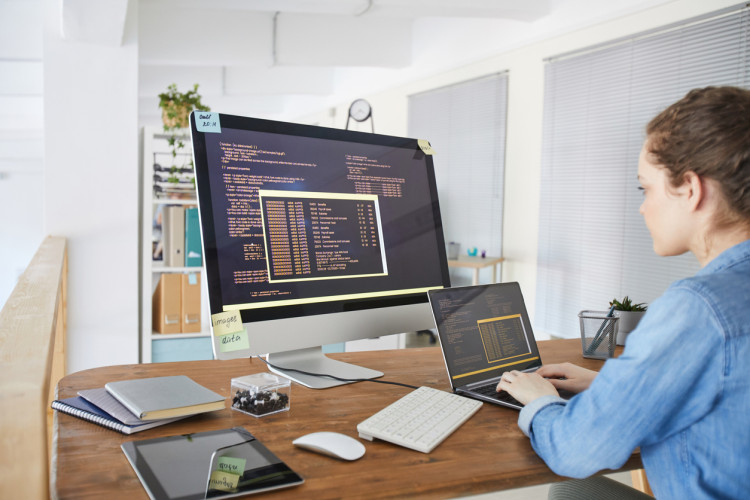 An algorithm developer works on multiple screens at a workstation.