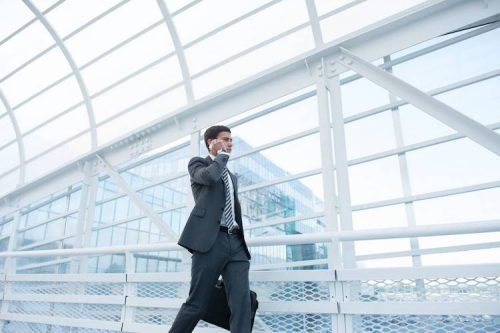 A man in a suit walks through an airport while talking on a cellphone.