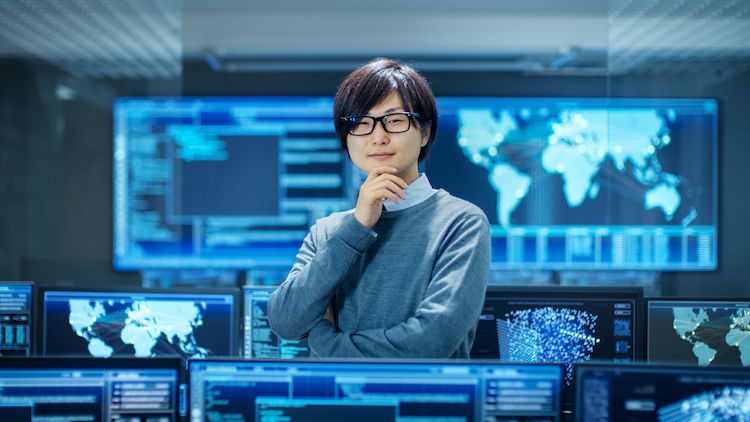 A chief security officer stands in a room surrounded by monitors and large screens of geographical locations.