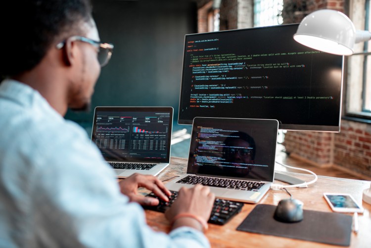 man looking at three computer screens with code