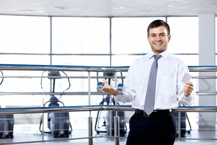 A smiling facilities manager in a white shirt and tie is standing in front of exercise equipment. 