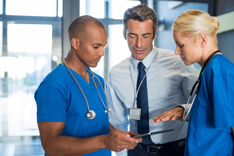 Medical team interacting using digital tablet at modern hospital. Mature doctor and african surgeon working on digital tablet with nurse. Head physician working with his medical team at clinic.