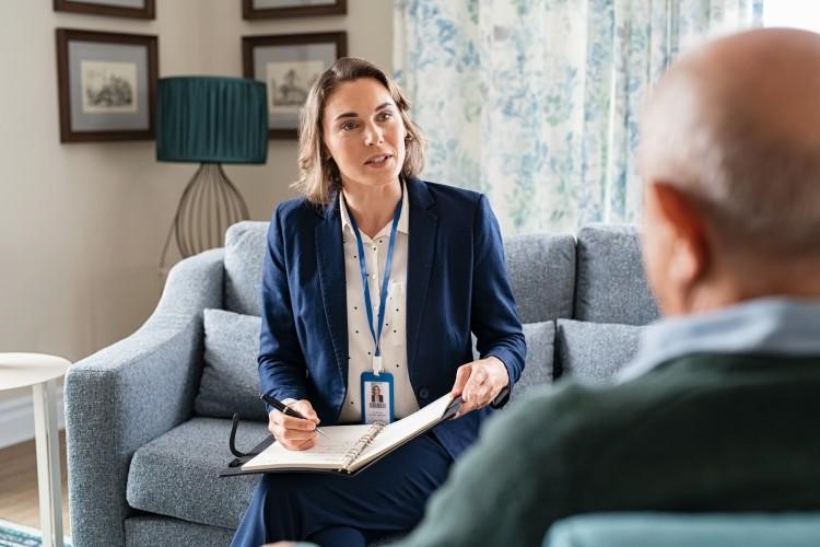 Healthcare social worker sitting with an elderly patient and taking notes.