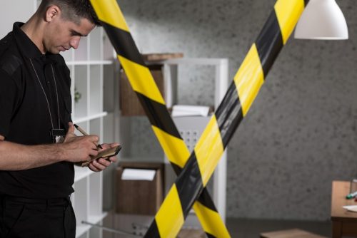 A criminal investigator writes on a notepad at crime scene blocked off with caution tape.