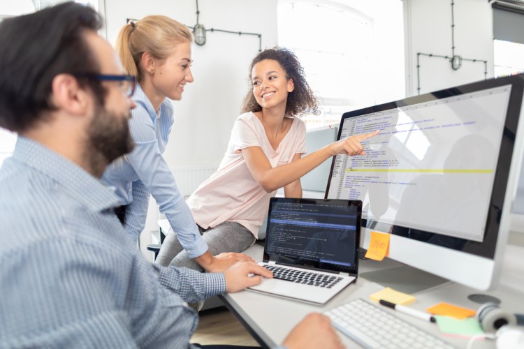 A smiling Java programmer points out a line of code on a monitor to a colleague. 