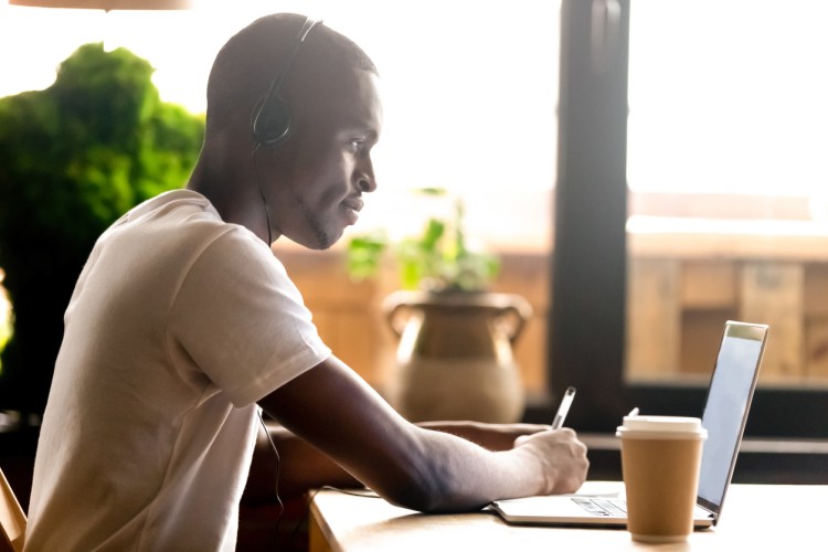 A student taking notes while attending an online class. 