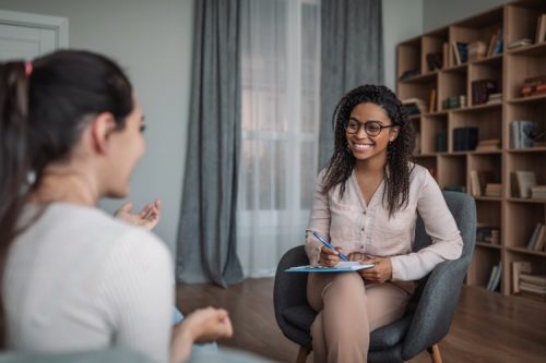 A seated therapist with a notebook and pen talks with a client.