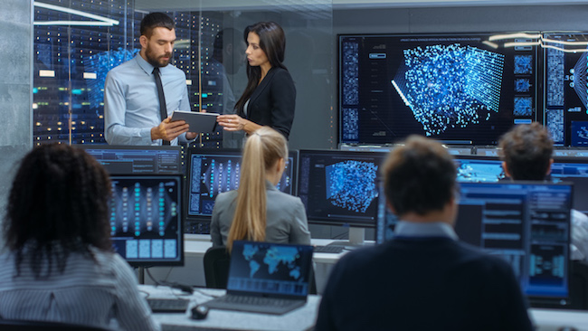 A director of security advises his team manager in a room full of computer monitors