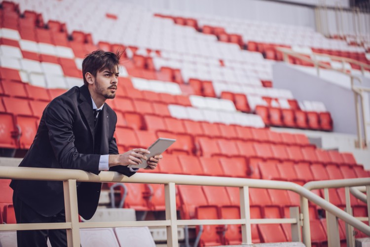 A sports agent watches their client from the bleachers.