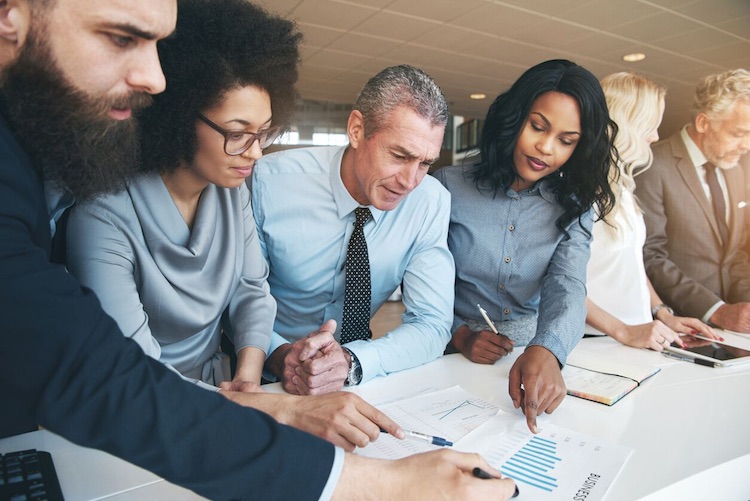 Co-workers gather around table in an office and analyze data charts