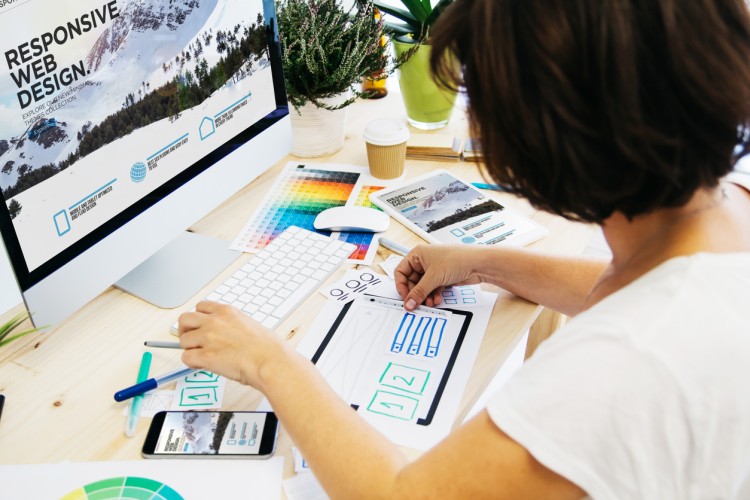 A web designer evaluates the website layout on a desktop computer, tablet, and smartphone.