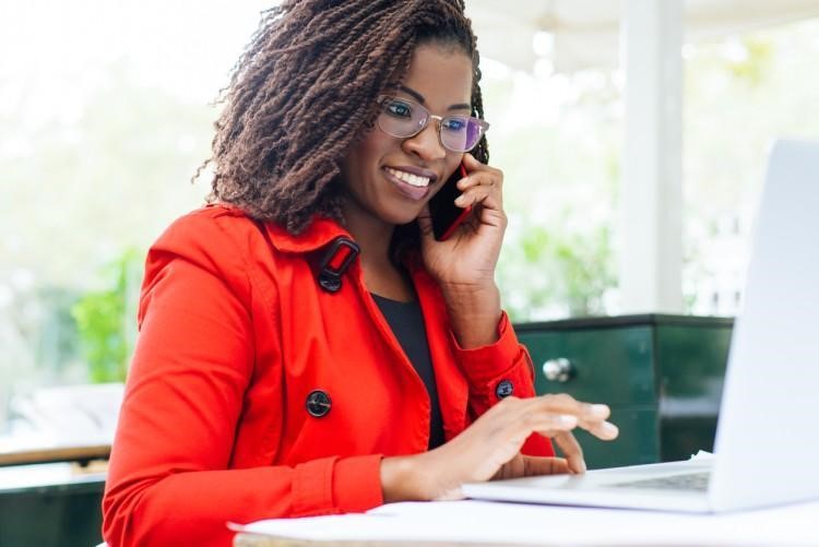 A smiling management consultant talks on the phone while using a laptop.