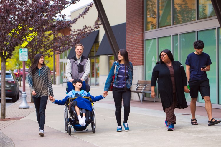 Two youth workers are walking down a city street with three teenagers and a boy in a wheelchair