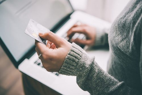 woman holds credit card while typing on laptop