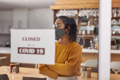 A masked server stands in a closed restaurant.