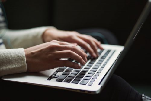 A person wearing a white shirt typing on a laptop.