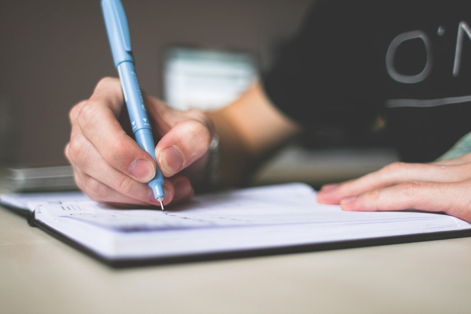  A close up of a person holding a blue marker or pen over a notebook.