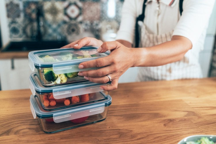 A person stacks storage containers of food.